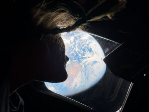 NASA astronaut and Artemis II mission specialist Christina Koch peers out of one of the Orion spacecraft’s main cabin windows, looking back at Earth, as the crew travels towards the Moon. Credit: NASA